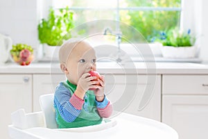 Baby boy eating apple in white kitchen at home