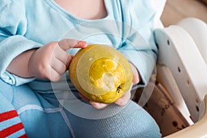 Baby eating fruit. Little boy biting apple sitting in white high chair in sunny kitchen with window and sink. Healthy nutrition