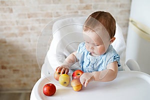 Baby eating fruit. Little girl biting yellow apple sitting in white high chair in sunny kitchen. Healthy nutrition for kids. Solid