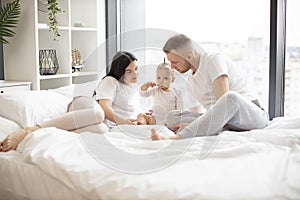 Baby eating with spoon while parents sitting on bed indoors