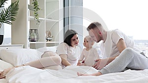 Baby eating with spoon while parents sitting on bed indoors