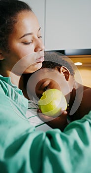 The baby eats an apple sitting in her mother's arms