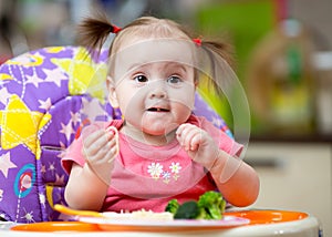 Baby eats pasta with vegetables sitting in highchair in kitchen