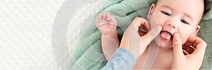 Baby face massage banner with copy space. Mother gently stroking baby boy face with both hands. Close up. Baby smiling.