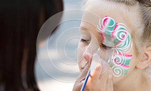 Little girl getting her face painted by face painting artist. photo