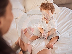 Baby, family and child clapping hands, happy and having fun on bed playing with his mother at home. Cute kid, son or