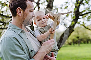 Baby and father holding wind turbine model, outdoors in park. Concept of renewable wind energy, sustainable future for