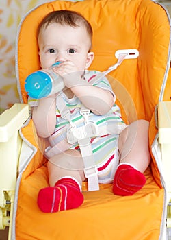 Baby with feeding-bottle sitting on highchair