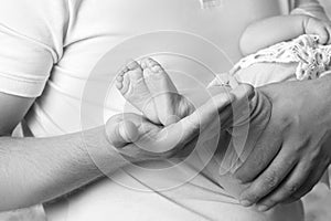 Baby feet in father hands. Tiny newborn baby's feet on male hands closeup. Dad and his child. Black-and-