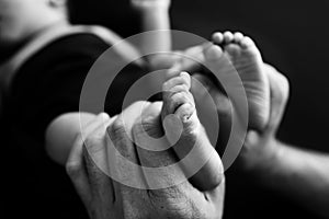 Baby feet in mother hands Mom her Child. Black and white photo, black background