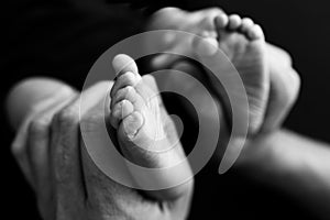 Baby feet in mother hands. Mom and her Child Black white photo, black background