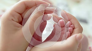 Baby feet in mother hands. Tiny Newborn Baby`s feet on female Heart Shaped hands closeup. Mom and her Child. Happy