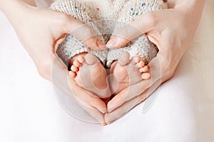 Baby feet in mother hands. Tiny Newborn Baby`s feet on female Heart Shaped hands closeup. Mom and her Child. Happy Family concept