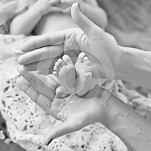 Baby feet in mother hands. Tiny Newborn Baby`s feet on female Shaped hands closeup. Mom and her Child