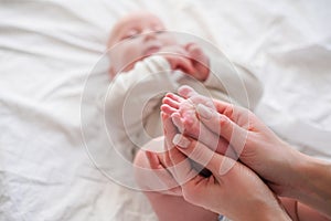 Baby feet in mother hands. Young caucasian woman makes massage for happy infant baby on white bed at home. Babycare