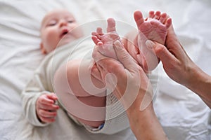 Baby feet in mother hands. Young caucasian woman makes massage for happy infant baby on white bed at home. Babycare photo