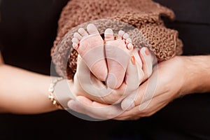 Baby feet in parents hands. Tiny Newborn Baby`s feet on parents shaped hands closeup. Parents and they Child. Happy Family concep