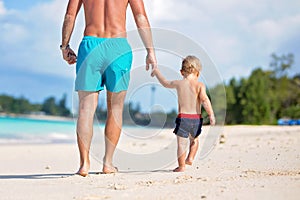 Baby feet in sand, dad and toddler walking on the beach