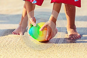 Baby feet walking on sand beach grabbing rugby ball, playful toddler wearing inflatable armbands hand holding ball