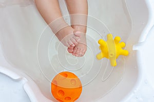 Baby feet in a white bathtub with toys