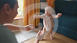 Baby first steps. Dad helps a baby toddler take first steps at home. Happy family kid dream concept. Baby boy learning