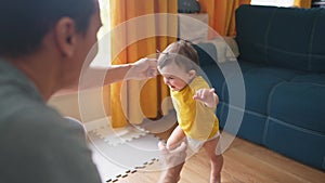 baby first steps. dad helps a baby toddler take first steps at home. happy family kid dream concept. baby daughter