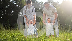 baby first steps. family walking in the park. mom and dad teach two babies the first steps on grass in the park. happy
