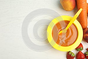 Baby food in bowl and fresh ingredients on white wooden table, flat lay. Space for text