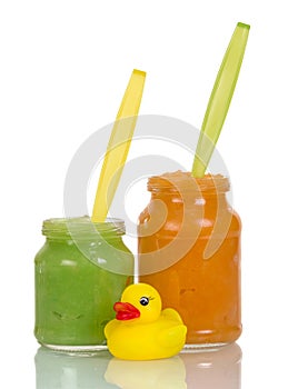 Baby food, fruit purees in jars next toy duck isolated on white