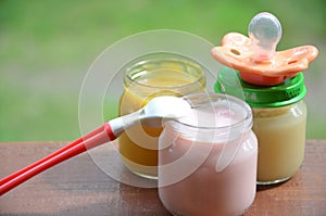 Baby food in jars puree mashed food on a background of foliage, With a pacifier and spoon