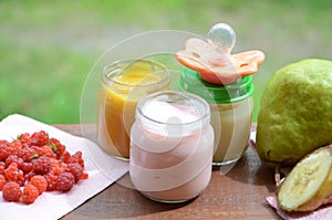 Baby food in jars puree mashed food on a background of foliage, With a pear banana, pacifier and a spoon