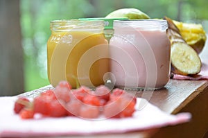 Baby food in jars puree mashed food on a background of foliage, With a pear banana, pacifier and a spoon