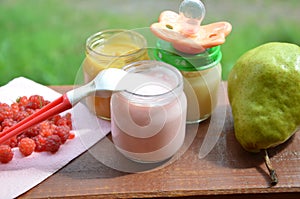 Baby food in jars puree mashed food on a background of foliage, With a pear banana, pacifier and a spoon