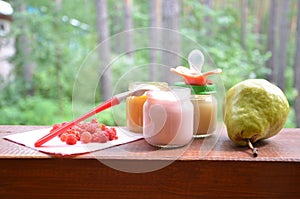 Baby food in jars puree mashed food on a background of foliage, With a pear banana, pacifier and a spoon