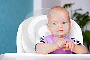 baby food. little smiling caucasian baby girl in pink bib on highchair at home. looking at camera. Newborn infant kids