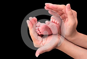 Baby foot in mother hands on black background