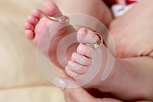 Baby foot in mother`s hands with care with rings on toes