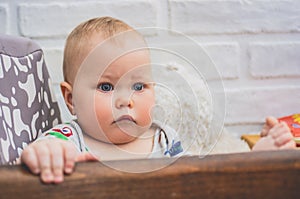 A baby with a frightened worried look sits on a chair