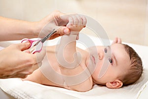 Baby getting fingernails cut by his mother with scissors while lying on his back. Nursing a child