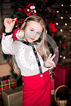 Baby girl 4-5 year old posing in room over christmas tree with decorations. Looking at camera. Merry christmas. Wearing stylish dr
