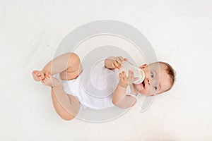 Baby girl 6 months old drinking milk from a bottle, lying on the bed in the nursery, feeding the baby, baby food concept