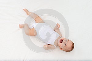 Baby girl 6 months old lying on the bed in the nursery on her back upside down, baby morning, baby products concept