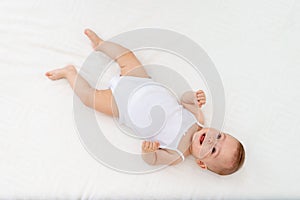 Baby girl 6 months old lying on the bed in the nursery on her back upside down, baby morning, baby products concept
