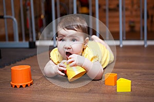 Baby girl 7 months old chewing on teething toy, while lying on hardwood floor