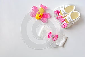 Baby girl accessories background. Pink butterfly teether, booties, headband  on a white table.