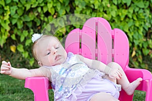 Baby Girl attempting to sit in chair outdoors, leaning over