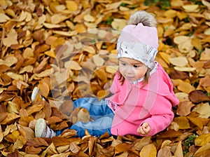 Baby girl in autumn park sitting in pile of dry leaves having fun. Autumn theme