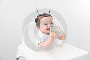 Baby girl in baby chair drinking water from baby bottle on white background