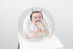 Baby girl in baby chair drinking water from baby bottle on white background