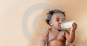 baby girl with beautiful curly hair, sitting and sucking milk from milk bottle